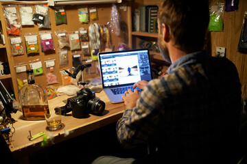 Downloading some photographs. Shot of a man using his laptop while working in his fly fishing...