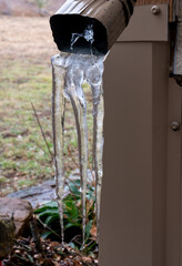 Icicle Fingers hang from a downspout at the corner of a house