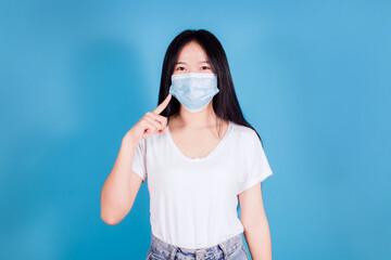 Portrait of asian teenager wearing and pointing a medical face mask to protect Covid-19 (Coronavirus) on blue background