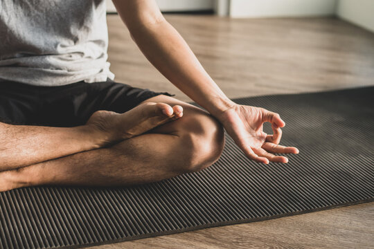 Young man sitting on the exercise mat practicing meditation in a lotus pose alone at the gym in the morning. He was closing his eyes, slowly breathing in and out.