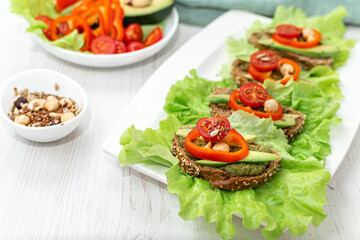 Sandwiches with rye bread, tomatoes, avocados, peppers and spicy sauce on a white plate covered with lettuce. Diet breakfast. healthy eating. Vegan snack Side view, close-up