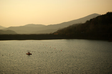 A large lake and a small boat surrounded by mountains at sunset.