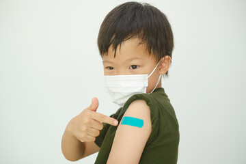 Doubtful child after getting a vaccine. Little kid wearing medical mask showing his arm with...