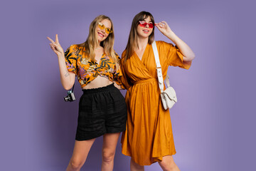 Two pretty women , best friends, posing on purple background in trendy  summer outfit.