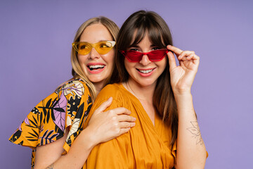 Close up portrait of two stylish women in sunglasses  and trendy summer clothes posing on purple...