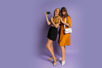 Two pretty women , best friends, posing on purple background in trendy  summer outfit. Full lenght.