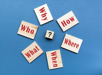 5 Ws and 1 H questions on wooden block cube against blue background.