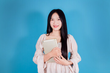 Beautiful young Asian businesswoman holding digital tablet while standing on blue background
