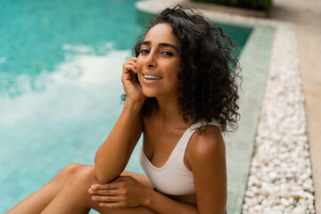 Fototapeta na wymiar Close up portrait of smiling tann woman with curly hairs posing in swimming pool . Summer and vacation concept.