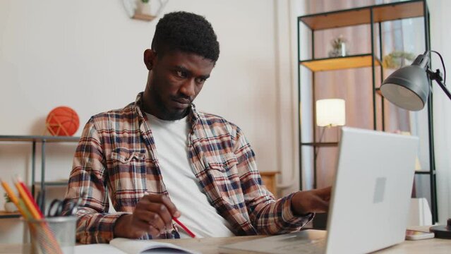 African american man freelancer using laptop computer sitting at desk working from home office. Adult guy businessman e-learning, browsing internet, online shopping, remote job on pc in living room