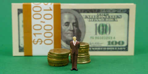 Miniatures. On the green surface is a pack of dollars, coins and a miniature figurine of people.