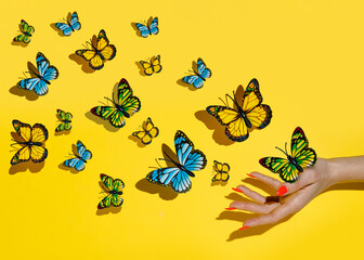 Butterflies flies free from women's hand against vibrant yellow background. Creative concept of...