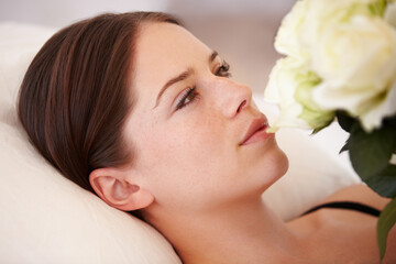 Her heart is won. A beautiful young woman lying down and admiring the bouquet of white roses she is holding.