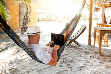 man with hat uses laptop remotely at the beach, near cabin. Playa La Ventanilla
