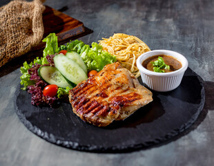 Grilled Boneless Chicken Steak with chili sauce, salad, noodles in a dish side view on dark background
