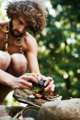 Creating fire. A young caveman trying to create fire using two stones, some leaves and wood.