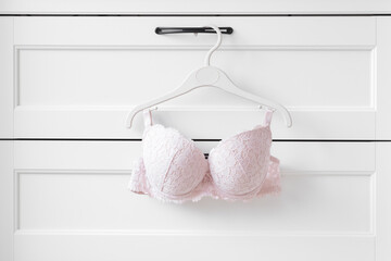 Light pink lace bra hanging on hanger at white drawer. Daily female underwear. Closeup. Front view.