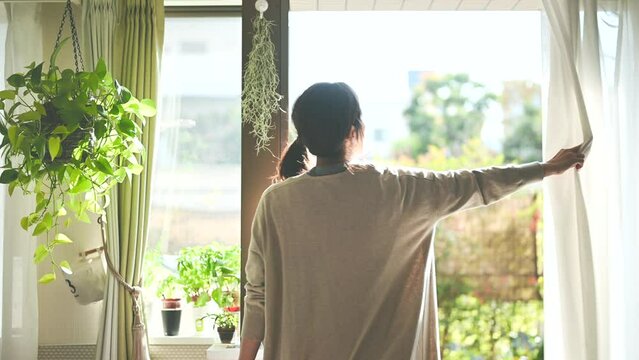 部屋のカーテンを開けて日光を浴びる女性