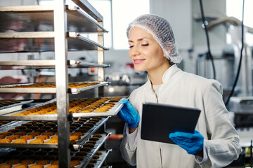 Satisfied female food factory inspector with tablet checking on baking products quality.
