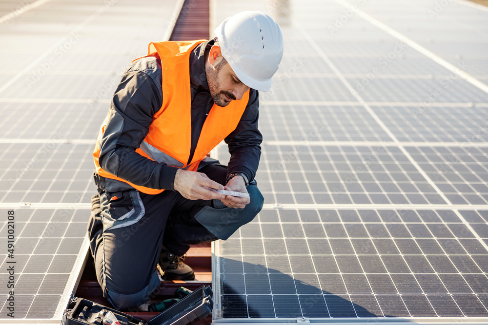 Wall mural A worker on the rooftop picking screws from toolbox to install solar panels.