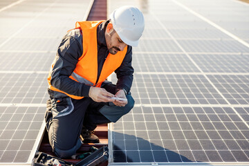 A worker on the rooftop picking screws from toolbox to install solar panels.