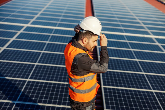 A Worker Putting Helmet While Standing On The Roof With Solar Panels.