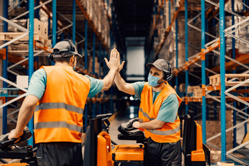 Two delivery service workers with voice picking headset on forklifts giving high five for...