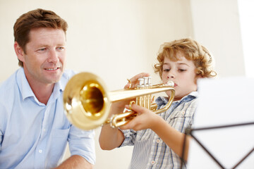 Proud of his little trumpet player. Shot of a cute little boy playing the trumpet while his father watches him proudly. - obrazy, fototapety, plakaty