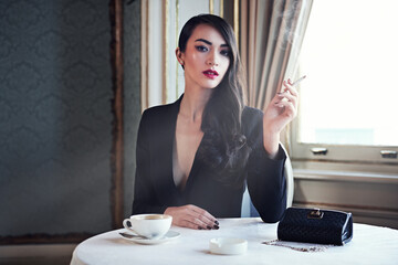 Luxury and style. Shot of a woman smoking a cigarette in a luxurious setting wearing classicly...