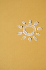 Close up funny sun made of make up cosmetic cream smudge on bright yellow background. Minimalist...