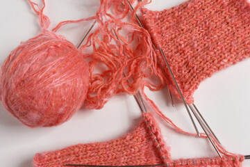 The knitting project is under implementation. A piece of knitting with a ball of yarn and knitting needles on a white background