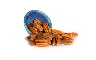 Pecan Halves Spilling from a Small Blue Pottery Bowl Isolated on White