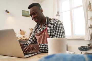 Joyous potter working on laptop in studio