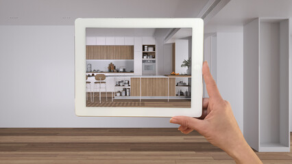 Augmented reality concept. Hand holding tablet with AR application used to simulate furniture and design products in empty interior with parquet floor, kitchen and dining room