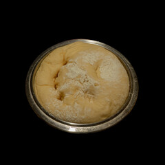 Yeast dough with flour in a bowl on a black background.