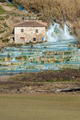 The beautiful natural thermal springs of Saturnia Cascate del Mulino, Grosseto, Tuscany, Italy, next to a typical stone cottage