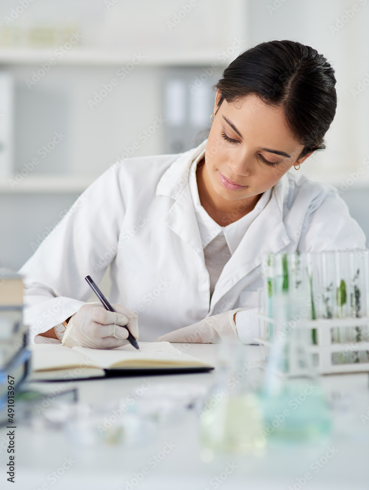 Poster Working on a new theory of hers. Shot of a young scientist writing notes while working in a lab.