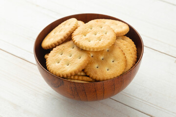 Rounded cracker cookies in a wooden bowl on white wooden table background.