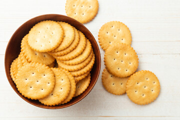 Rounded cracker cookies in a wooden bowl on white wooden table background.
