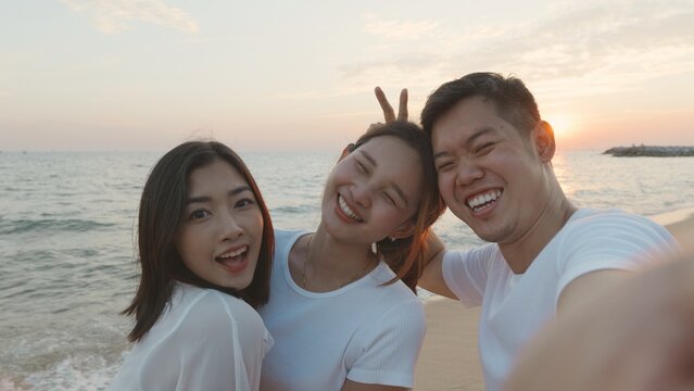 Happy friends smiling and posing taking selfie from smartphone and having fun together on beach in holiday vacation time at sunset, Young Asian group woman and man in summer travel outdoor