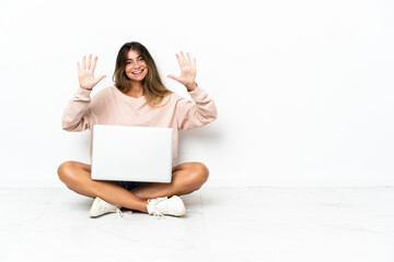 Young woman with a laptop sitting on the floor isolated on white background counting ten with fingers