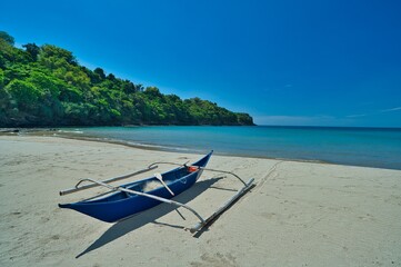 Small boat in sunny blue sky landscape view of beach resort area on white sand in Philippines