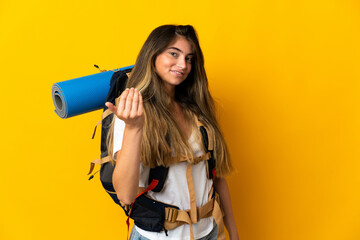 Young mountaineer woman with a big backpack isolated on yellow background inviting to come with hand. Happy that you came