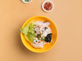Thai food Sliced Fish Porridge in a bowl with soup, chili sauce and spring onion top view on wooden table