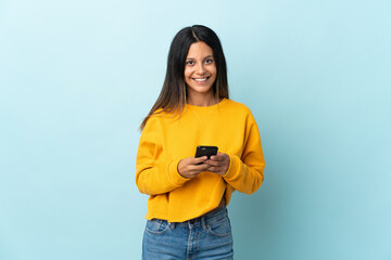 Caucasian girl isolated on blue background sending a message with the mobile