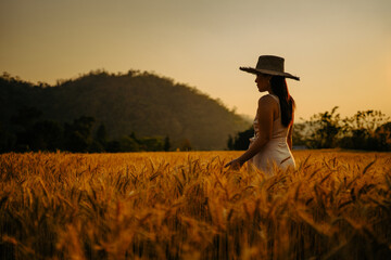 Young woman standing on ripe wheat field at dusk.