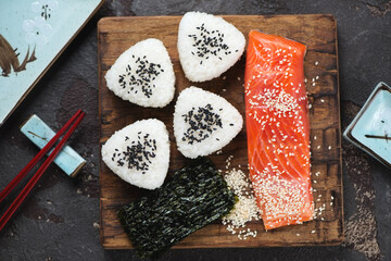 Onigiri or rice formed into triangular shapes with salmon and nori sheets on a rustic wooden chopping board, view from above, middle close-up
