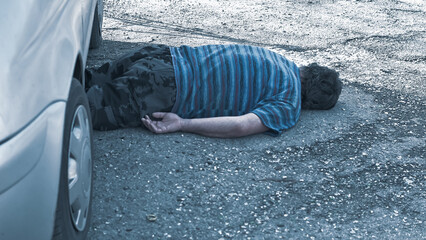 the body of a dead man lies under a car on the road after a car crash