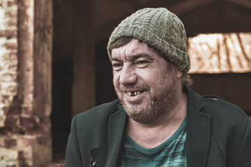 a poor homeless man in a hat and suit smiles looking at the camera in modern society , the concept...
