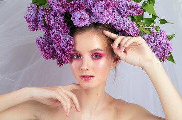 Portrait of a young girl in the studio with lilac flowers on her head, close-up. Creative beautiful make-up in doll style with lilac flowers on the head close-up.